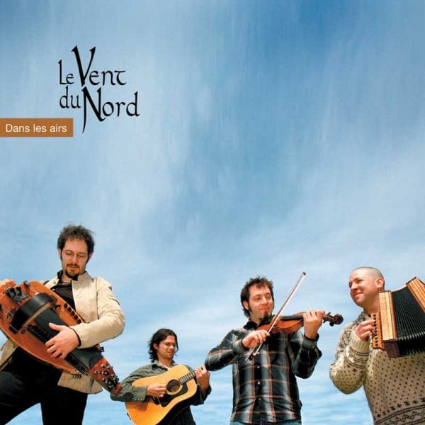 A group of men from Le Vent du Nord - Dans les airs are standing in front of a blue sky with their instruments.