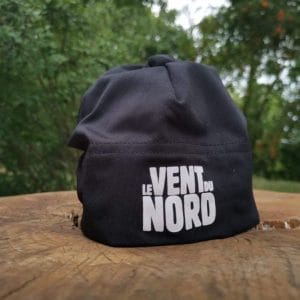 A black cap with the phrase "le vent du nord" printed on it, placed on a wooden surface outdoors.